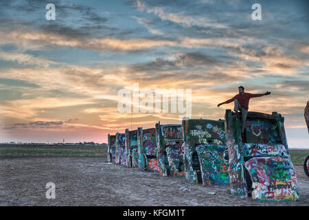 Amarillo, Texas, USA. Oktober 2015. Mann sitzt auf einem cadillac mit offenen Armen auf der Cadillac Ranch während Sonnenaufgang. Stockfoto