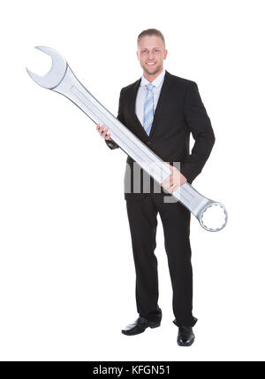 Schöne bärtige Geschäftsmann in einem eleganten Anzug mit einem großen Schraubenschlüssel in der Hand konzeptionelle Lösung des Problems isoliert auf weiss Stockfoto