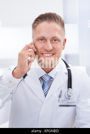 Freundliche Arzt plaudern auf seinem Handy lächelte, als er auf dem Gespräch in der Nähe von seinem Gesicht hört Stockfoto