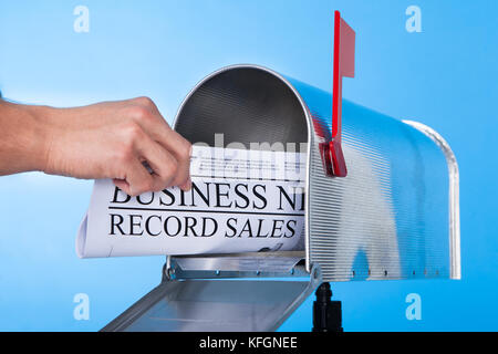 Mann sein Postfach zu öffnen, um e-Mails im Inneren schließen sich seine Hand auf die offene Tür vor einem blauen Himmel entfernt Stockfoto