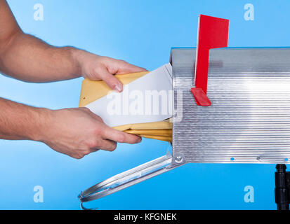 Mann sein Postfach zu öffnen, um e-Mails im Inneren schließen sich seine Hand auf die offene Tür vor einem blauen Himmel entfernt Stockfoto