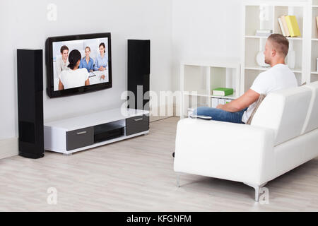 Mann sitzt auf einem Sofa in seinem Wohnzimmer vor dem Fernseher allein zu Hause Stockfoto