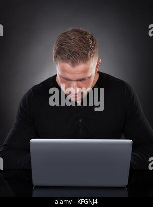 Ein Mann oder Hacker, der nachts an einem Laptop arbeitet und sich im Schein des Bildschirms über die Tastatur beugt, während er im Internet oder im Internet surft Stockfoto