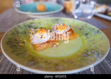 Zwei gebratene Wachtel Eier über Knödel auf grün Keramik Teller auf Unterlage im Restaurant Stockfoto