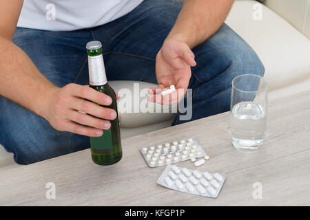 Mann sitzt auf der Couch auf Pillen und Flasche in der Hand halten Stockfoto