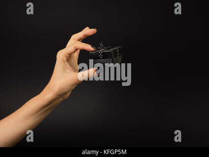 Weibliche Hand, die eine schwarze Geschenkbox mit schwarzen Band verziert mit weißen Tupfen. Auf schwarzem Hintergrund isoliert. Stockfoto