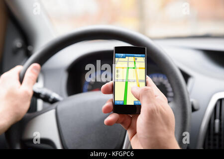 Nahaufnahme des Mannes mit GPS-Navigation im Mobiltelefon während der Fahrt mit dem Auto Stockfoto