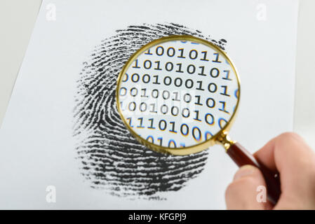 Person Hand mit Vergrößerungsglas über Einem Fingerabdruck enthüllt binären Code im Druck Stockfoto