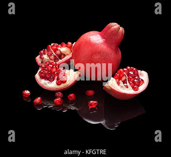 Granatapfel Obst mit Saatgut und Scheiben auf Schwarz glänzend Hintergrund mit echten Reflexion isoliert. Stockfoto