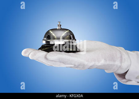 Nahaufnahme des Butlers hand Holding service Bell vor blauem Hintergrund Stockfoto