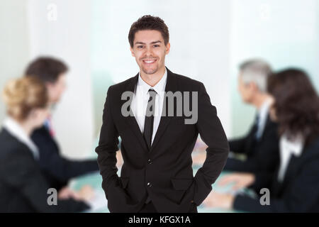 Portrait von stattlicher Junge Unternehmer stehen gegen Kollegen, die sich für Treffen im Büro Stockfoto
