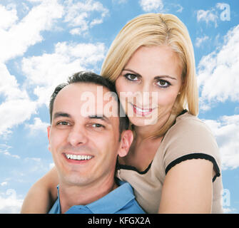 Portrait von glücklichen Mitte erwachsener Mann, piggyback Ride zu Frau gegen Sky Stockfoto