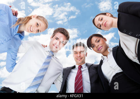 Low Angle Portrait von Multiethnischen Geschäft Leute bilden huddle gegen Sky Stockfoto