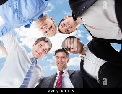 Low Angle Portrait von Multiethnischen Geschäft Leute bilden huddle gegen Sky Stockfoto