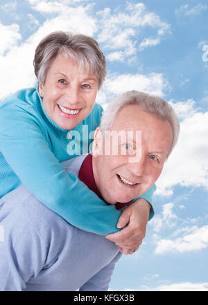 Portrait von Happy älterer Mann, piggyback Ride zu Frau gegen Sky Stockfoto