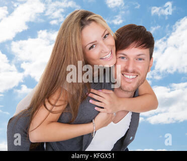 Porträt der glückliche junge Mann, piggyback Ride zu Freundin gegen Sky Stockfoto