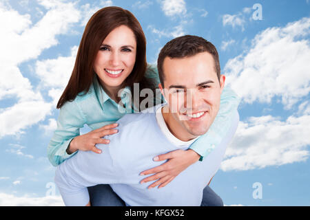 Portrait von glücklichen Mann, piggyback Ride zu Freundin gegen Sky Stockfoto