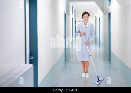 Volle Länge Portrait von Happy Reiniger aufwischen Stock im Krankenhaus Stockfoto