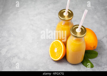 Orangensaft in Glasflaschen, frische Orangen auf grauem Beton Hintergrund Stockfoto