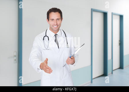 Portrait von Happy zuversichtlich Arzt mit Handshake halten Zwischenablage im Krankenhaus Flur Stockfoto