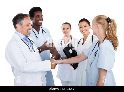 Ärzte machen Handschlag, während Kollegen sie auf weißem Hintergrund betrachten Stockfoto