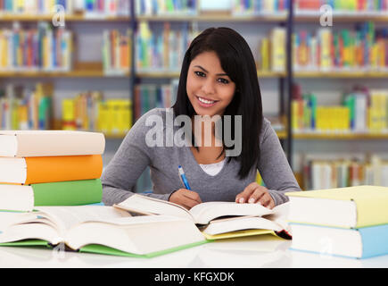 Porträt einer glücklichen weiblichen Studentin, die am Tisch in der Bibliothek studiert Stockfoto
