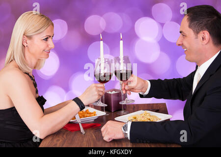 Romantisches Paar, das sich anschaut, während es Weingläser am Restauranttisch toaste Stockfoto