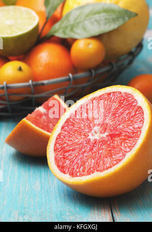 Eine Halbe Grapefruit und andere Zitrusfrüchte: Orange, Zitrone, Mandarine, Limette, kumquat auf einem blauen Hintergrund aus Holz Stockfoto