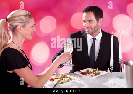 Lächelndes junges Paar, das sich anschaut, während es Champagner-Flöten am Restauranttisch toaste Stockfoto
