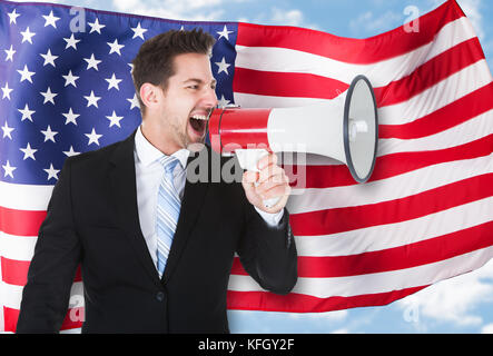 Porträt eines Geschäftsmannes Schreien über Megaphon vor der amerikanischen Flagge Stockfoto