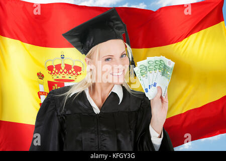 Weibliche Schulabgänger halten Geld vor der spanischen Flagge Stockfoto