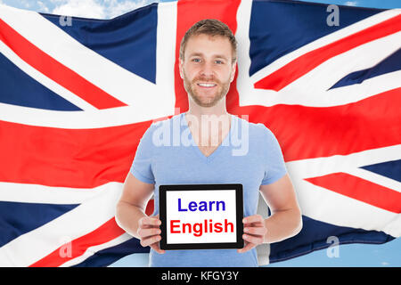 Junger Mann vor der britischen Flagge Holding digital Tablet mit Englisch lernen Text Stockfoto