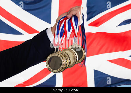 Nahaufnahme der Hand des Kaufmanns holding Medaillen vor der britischen Flagge Stockfoto