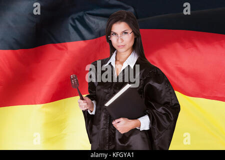 Selbstbewusste Richterin Mit Gesetzbuch Und Holzgavel, Die Vor Der Deutschen Flagge Steht Stockfoto