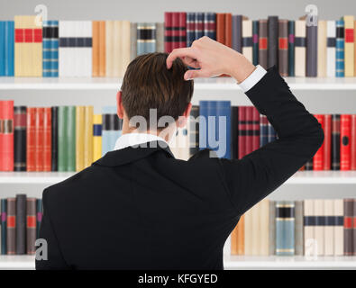 Rückansicht des Mannes in Einem Anzug, der seinen Kopf in der Bibliothek kratzt Stockfoto