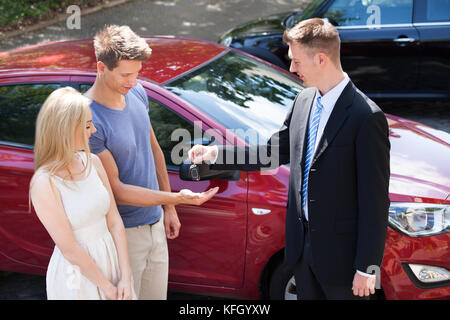 Junge Verkäufer geben Schlüssel zum Paar, das durch neue Auto Stockfoto