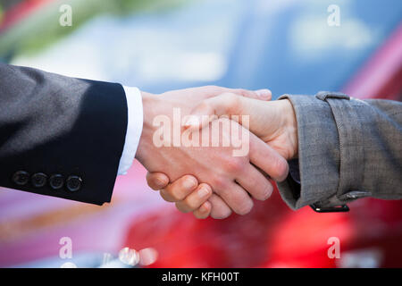 Zugeschnittenes Bild der Autohändler und weibliche Kunden Hände schütteln beim Händler Stockfoto