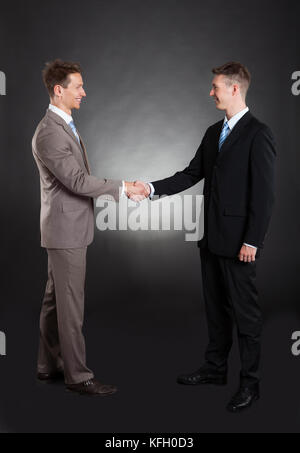 Gesamte Länge der lächelnde Geschäftsleute Händeschütteln vor schwarzem Hintergrund Stockfoto