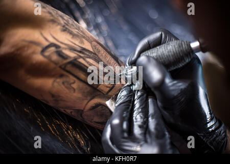 Ein professionelles Tattoo Künstler stellt schwarze Tinte in die Haut mit einer Nadel von einem Tattoo Maschine. Stockfoto