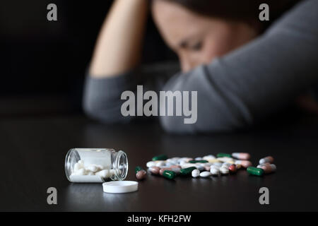 Nahaufnahme von einer depressiven Frau neben einer Menge Pillen auf eine Tabelle auf einem dunklen Hintergrund Stockfoto