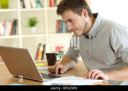 Ernsthafte Freelancer arbeiten im Hinblick auf die Überprüfung der Inhalte in einem Laptop auf dem Schreibtisch zu Hause Stockfoto