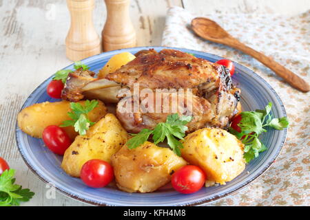 Ofen zubereitet Schweinefleisch Schaft mit Kartoffel, serviert mit frischen Tomaten und Petersilie. Stockfoto