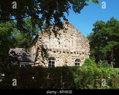 Ein Ferienhaus mit einer alten Steinmauer Fassade auf seinem eigenen Land unter Bäumen, Sträuchern und blauer Himmel. . Stockfoto