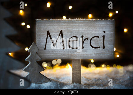 Schild mit französischen Text merci bedeutet Danke. weiß Weihnachtsbaum mit Schnee und Magic glühenden Lichter im Hintergrund. Karte für Seasons Greetings. Stockfoto
