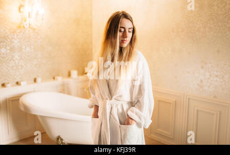 Junge Frau in weißem Bademantel, Badezimmer auf Hintergrund. Körperpflege und Hygiene, Gesundheitswesen Stockfoto