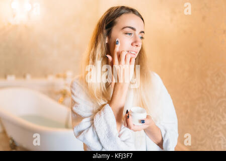 Lächelnde Frau in weißen Bademantel, Gesichtspflege im Badezimmer. Die Körperpflege und Hygiene, Gesundheitswesen Stockfoto