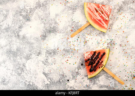 Scheiben Wassermelone in Eis Form. Beliebte Sommer Obst Wassermelone mit Puderzucker und Schokolade auf Stick. Wassermelone in popsicle Form. Ansicht von oben. Flach Stockfoto