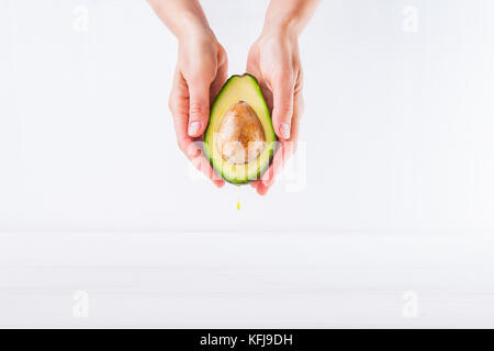 Frische Avocado mit Öl drop in weibliche Hände auf dem weißen Hintergrund isoliert. gesunde, natürliche Schönheit Konzept. Vorderansicht. Platz für Text Stockfoto