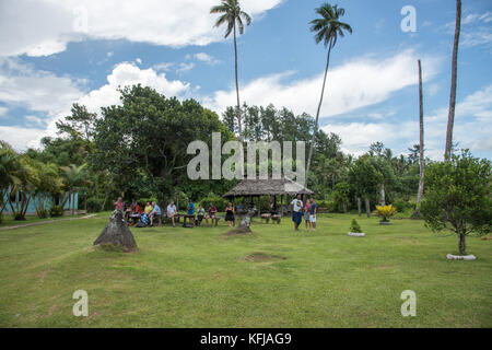 SUVA, VITI LEVU, FIDSCHI-28. NOVEMBER 2016: Touristen ruhen auf einer Bank in einem abgelegenen Dorf mit Strohdach und tropischer Flora in Suva, Fidschi Stockfoto
