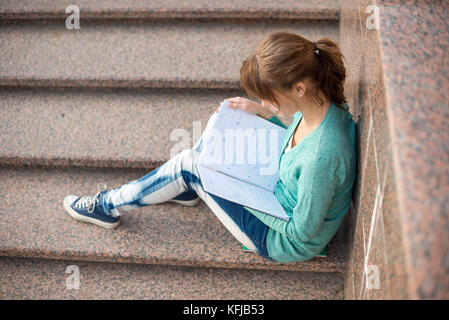 Mädchen auf der Treppe sitzen und lesen Hinweis Stockfoto